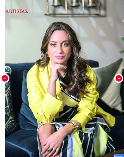 Close-up of Monica Varela, a Latin artist, in vibrant yellow and stylish outfit indoors.