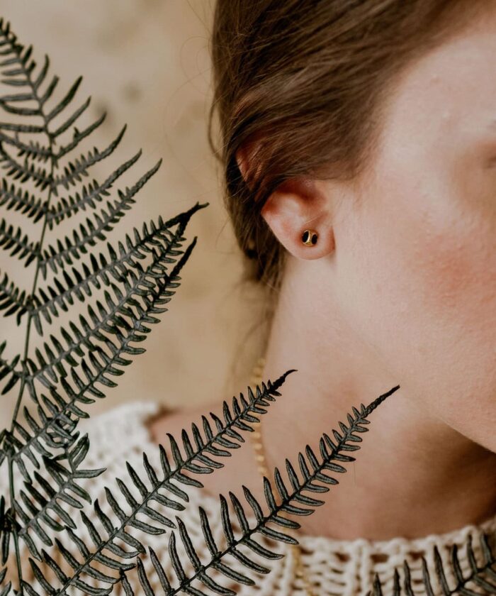 Close-up of Monica Varela's ear with black and gold earrings, framed by fern leaves.