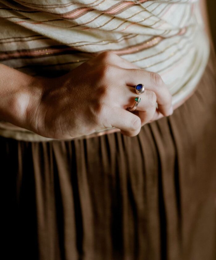 2. Close-up of delicate rings featuring colorful stones on a woman's finger, with a textured chair in the background.