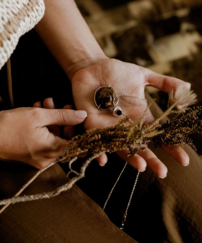 Hand holding a necklace with amber pendant and gemstone, cozy rustic background.