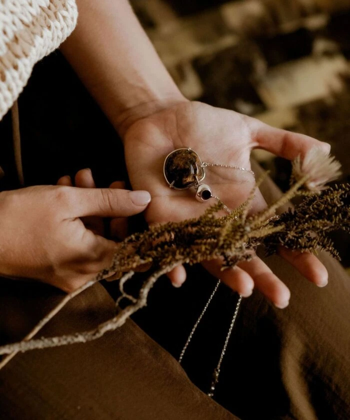 Hand holding a necklace with amber pendant and gemstone, cozy rustic background.