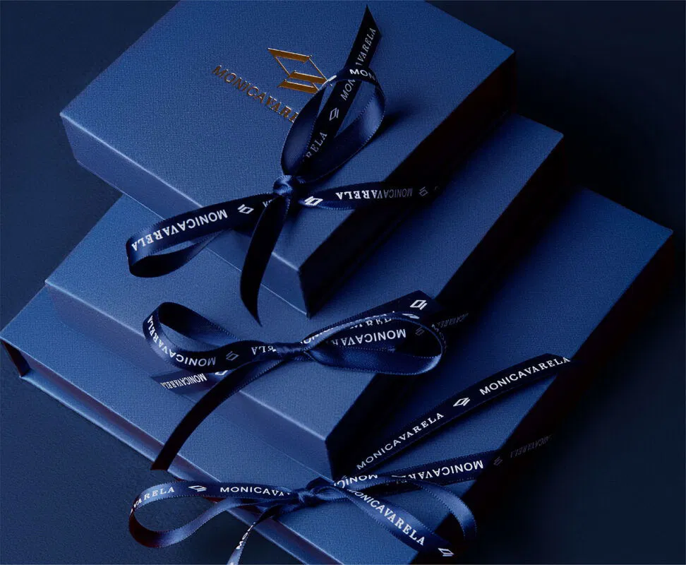 Luxurious navy blue gift boxes tied with satin ribbons bearing Monicavarelas logo, ideal for Valentine's Day gifts.