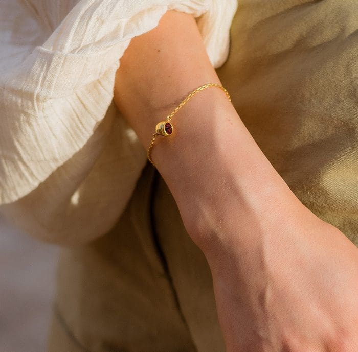 Delicate gold bracelet featuring a red gemstone charm, perfect for stylish accessories and jewelry lovers.