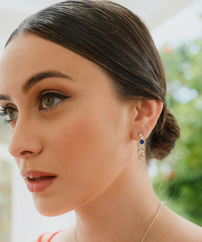 Close-up of Monica Varela wearing small silver and blue hoop earrings for a stylish and elegant look.