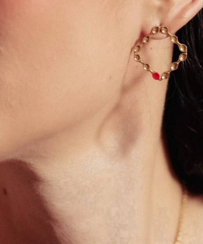Gold heart-shaped earring with red detail, close-up jewelry shot.