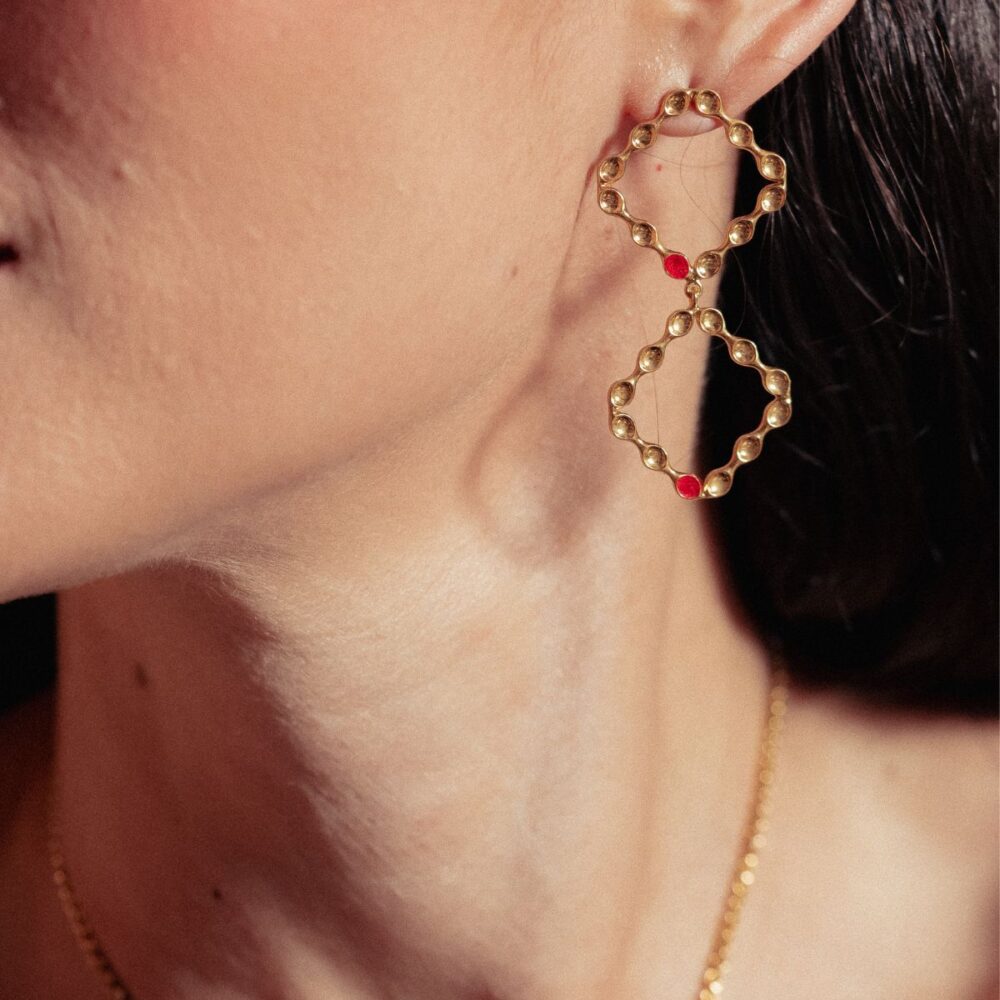 Daring gold infinity earrings with red embellishments, ideal for fashion-forward looks.
