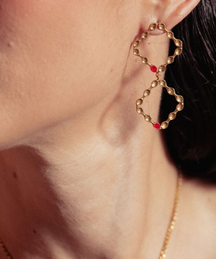 Daring gold infinity earrings with red embellishments, ideal for fashion-forward looks.
