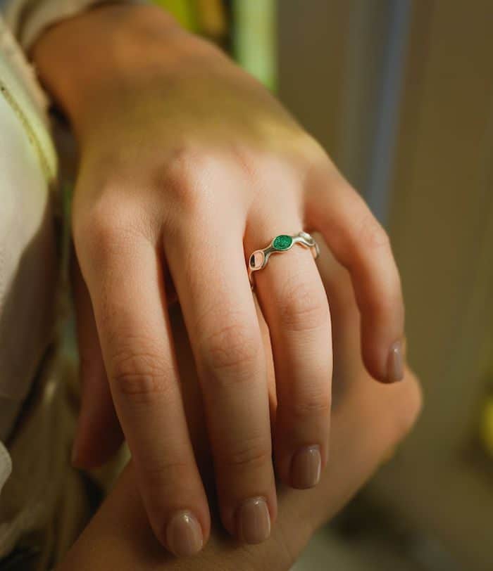 Close-up of a silver margin ring featuring a green gemstone on a woman's finger.