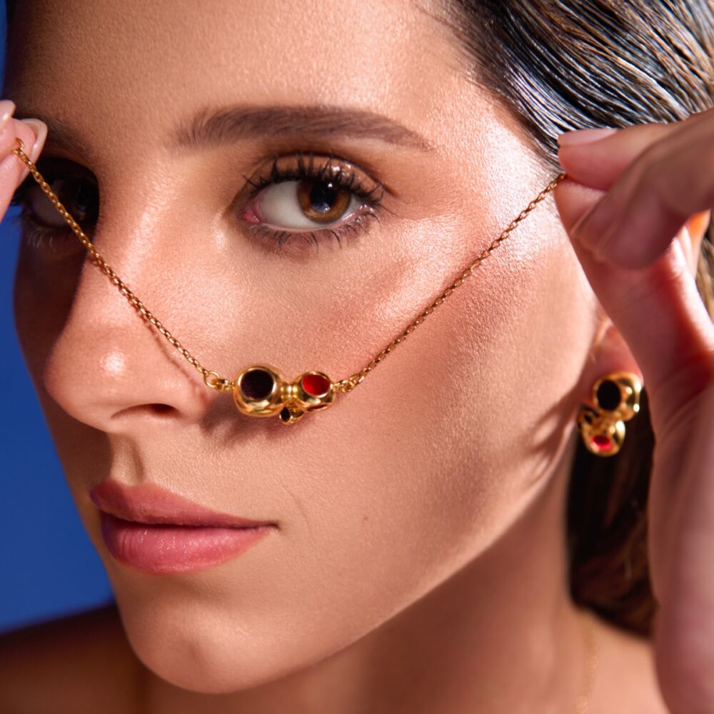 Close-up of a woman wearing a gold triad pendant necklace with red and black beads, paired with matching earrings.