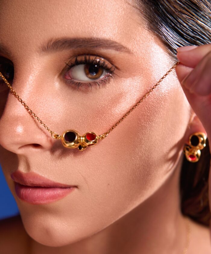 Close-up of a woman wearing a gold triad pendant necklace with red and black beads, paired with matching earrings.