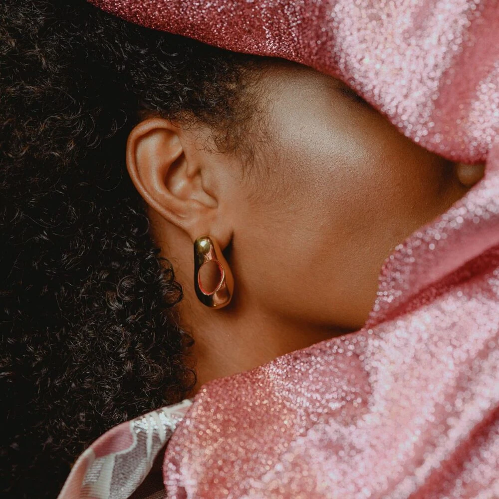 Close-up of gold hoop earring on a woman's ear, accentuated by pink glitter fabric.