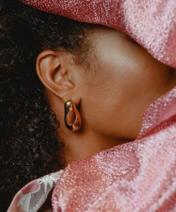 Close-up of gold hoop earring on a woman's ear, accentuated by pink glitter fabric.