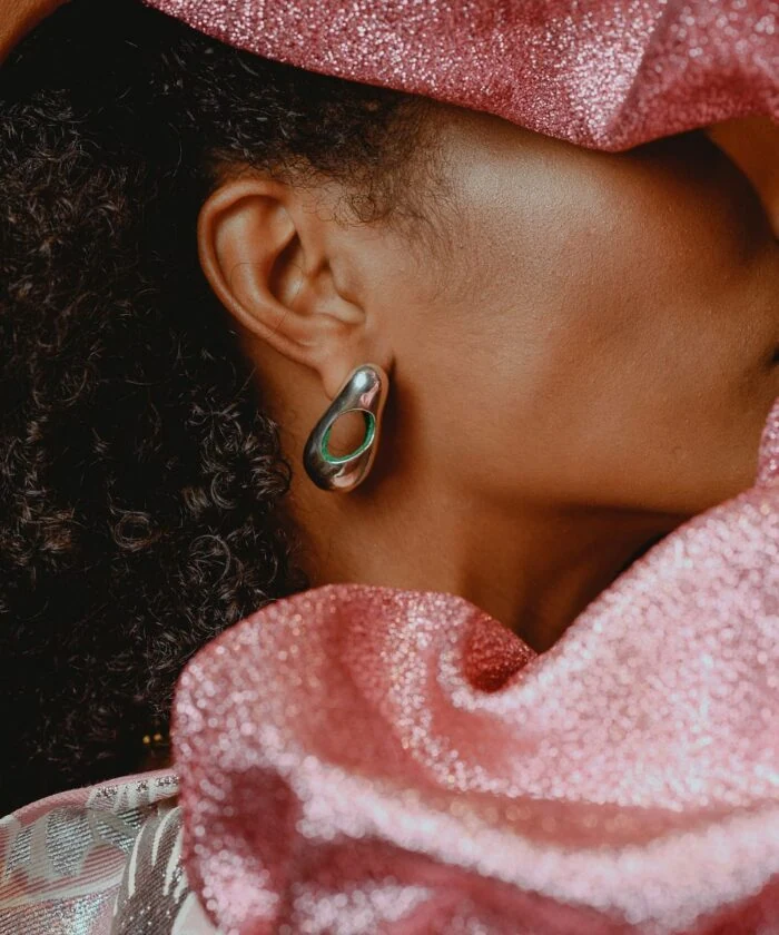 Close-up of a woman wearing a silver hoop earring with textured curls in her hair and pink glittery fabric.
