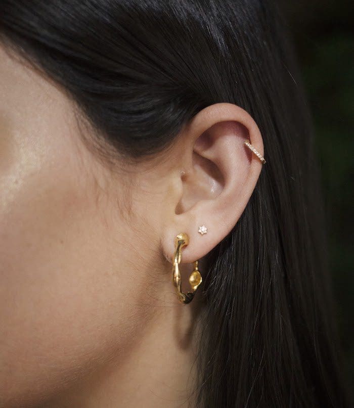 Close-up of ear showcasing gold hoops and delicate stacking earrings.