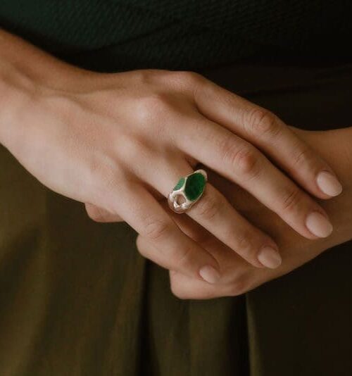 Close-up of a stylish silver magnet ring with green stone detail on a woman's finger.