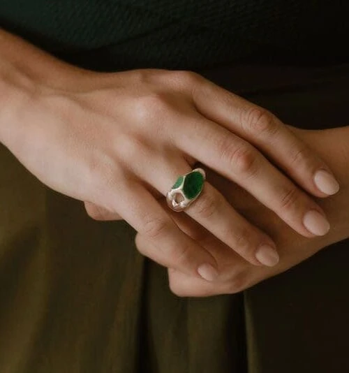 Close-up of a stylish silver magnet ring with green stone detail on a woman's finger.