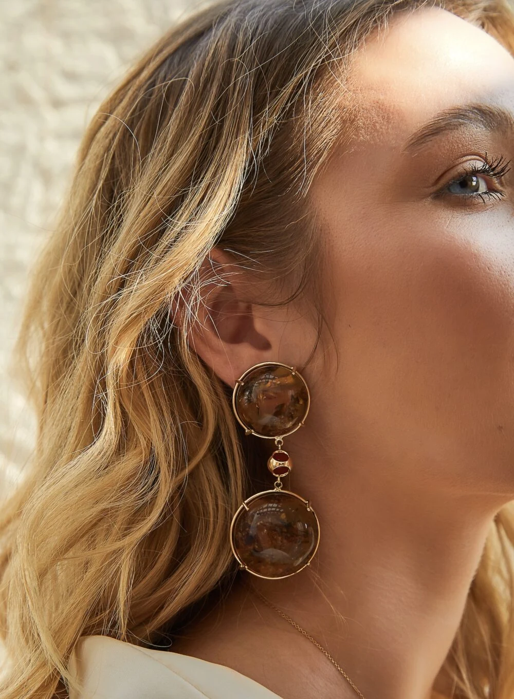 Close-up of a woman’s face highlighting her large earrings and radiant complexion. Fashion-forward look inspired by Monica Varela.