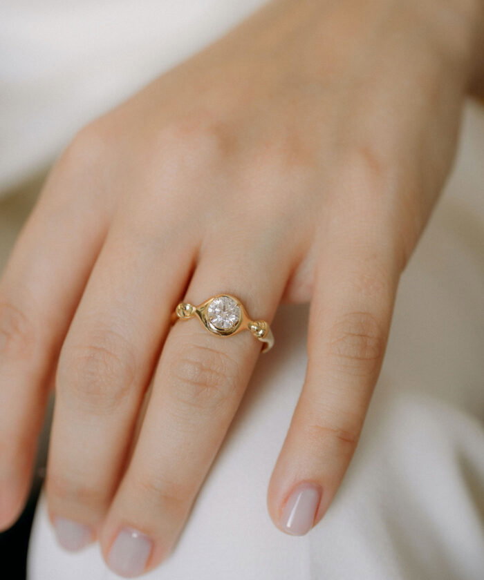 Close-up of a stunning gold ring featuring a central diamond on a woman's finger. Perfect for jewelry lovers.