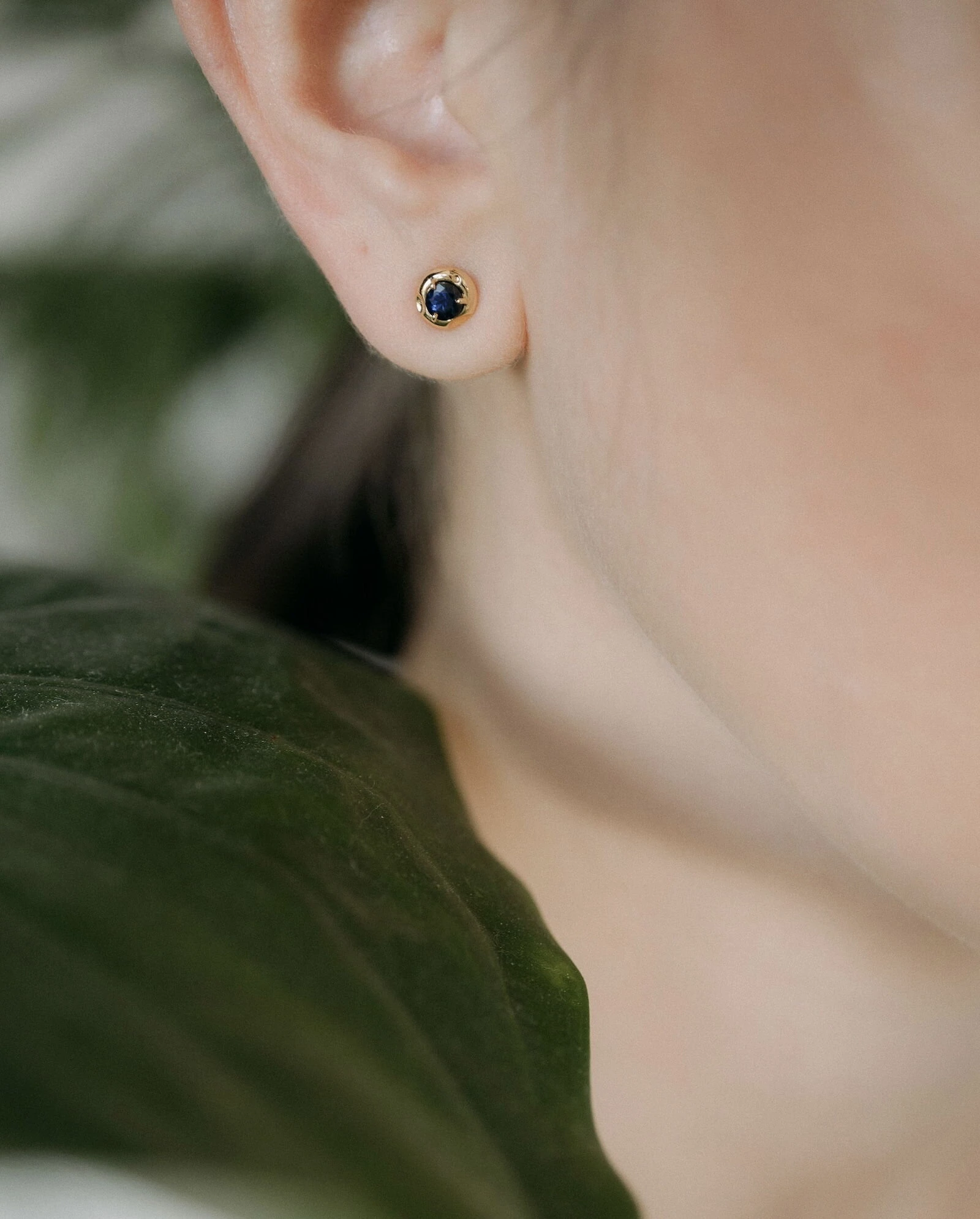 Elegant sapphire stud earrings for women Delicate gold and sapphire stud earrings on a woman's earlobe, showcasing luxury jewelry.