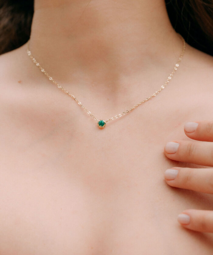 Close-up of a delicate gold chain necklace with a vibrant green emerald pendant on smooth skin.