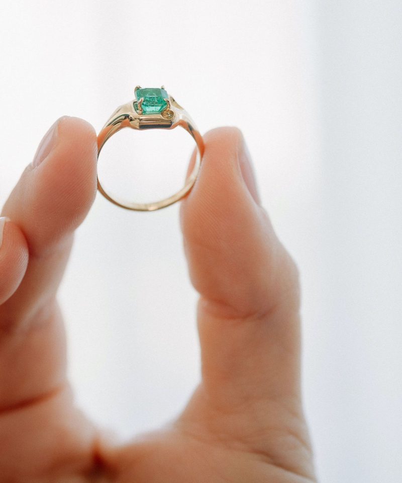 Anillo Fauli talla esmeralda en oro amarillo de 18k, sostenido entre los dedos
