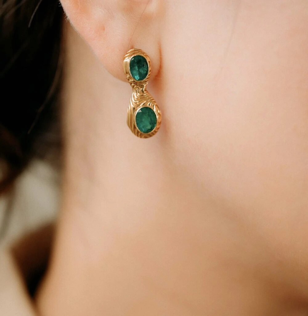 Gold earrings with striking green emerald stones, perfect for a stylish and sophisticated look.
