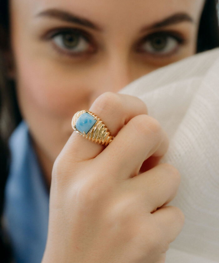Close-up of a gold larimar ring with blue gemstone, showcasing elegant jewelry design.