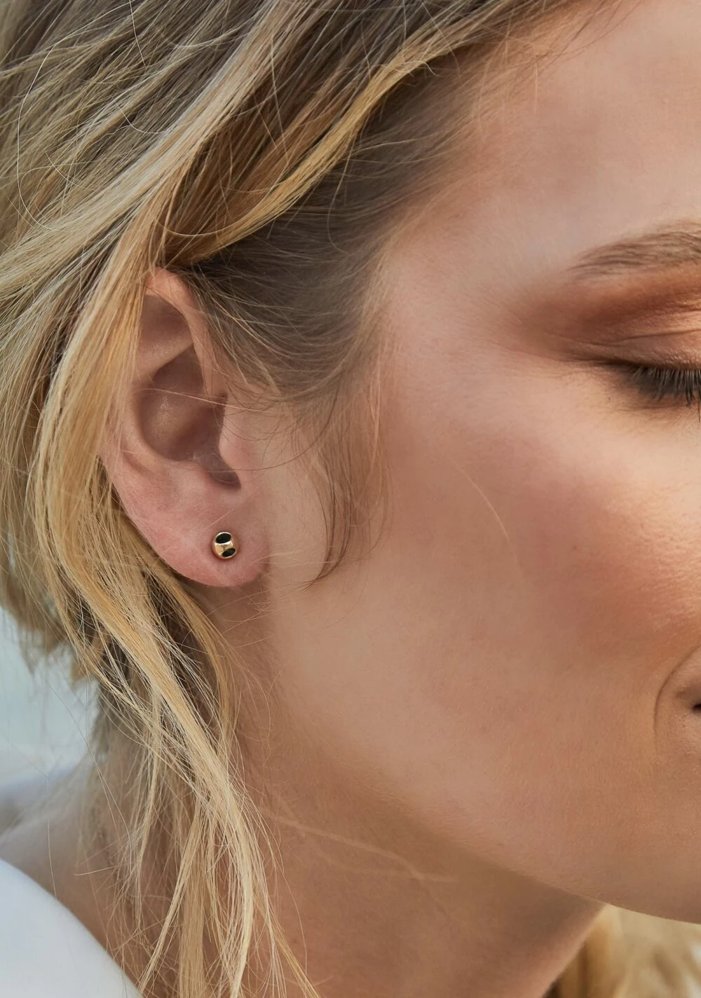 Elegant gold and black stud earring on a woman's earlobe.