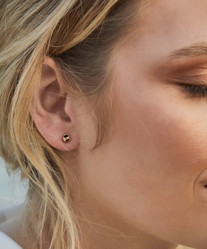 Elegant gold and black stud earring on a woman's earlobe.