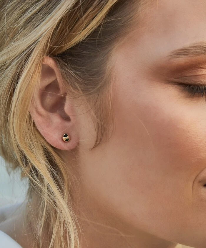 Elegant gold and black stud earring on a woman's earlobe.