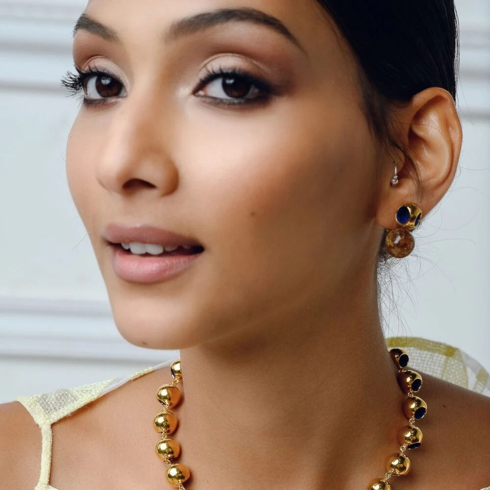 A close-up of a woman's ear with gold and gemstone stud earrings, showcasing luxury jewelry with dark red and brown details.