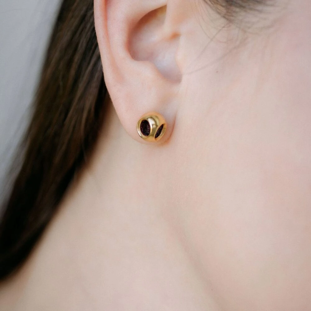 Luxurious gold jewelry earring with black detailing, close-up on the ear.