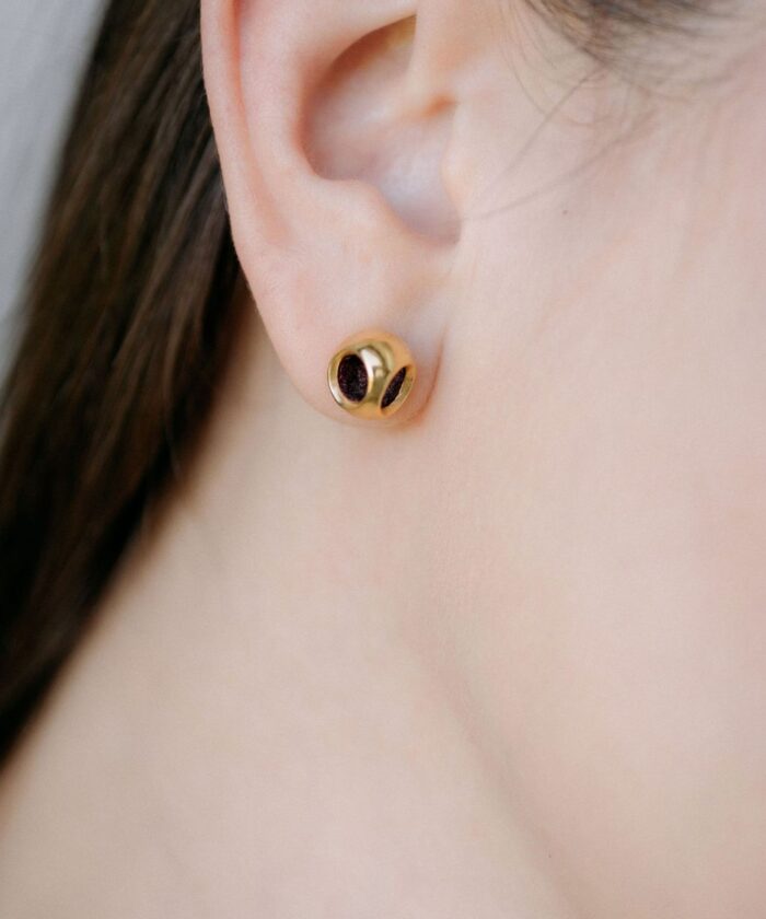 Luxurious gold jewelry earring with black detailing, close-up on the ear.