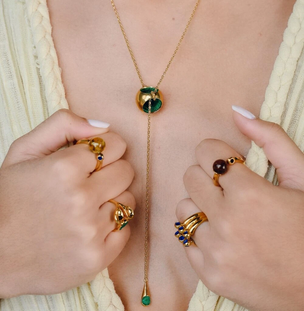 Stunning gold jewelry featuring green and brown stones, including rings and a necklace with a stylish knot T-necklace design.