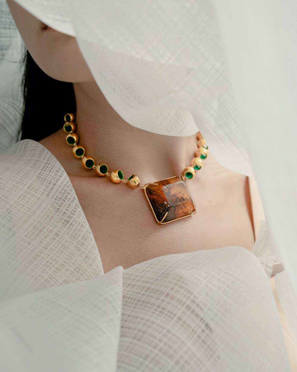Close-up of luxurious amber and gold necklace showcasing vibrant green accents on model's neck.