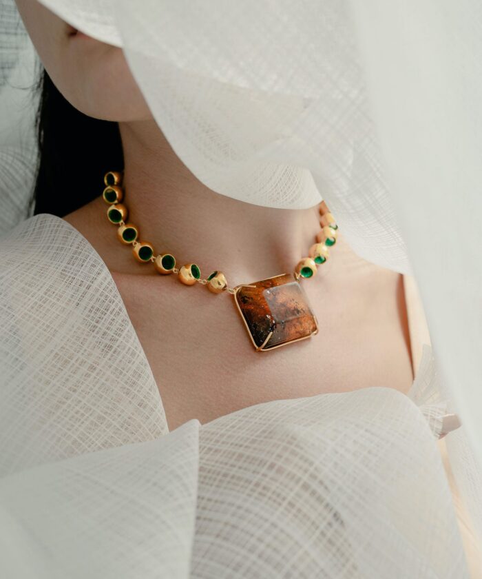 Close-up of luxurious amber and gold necklace showcasing vibrant green accents on model's neck.