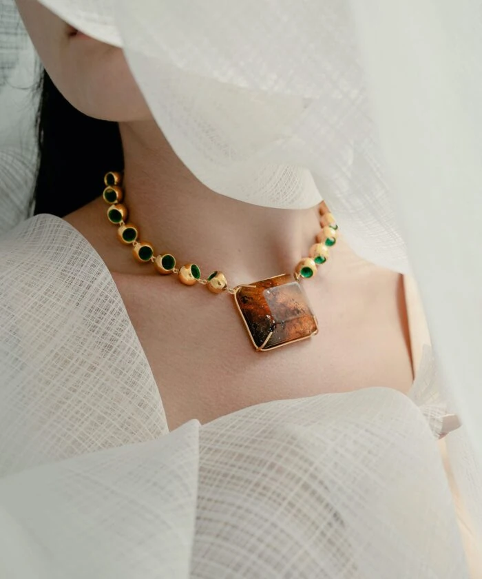 Close-up of luxurious amber and gold necklace showcasing vibrant green accents on model's neck.