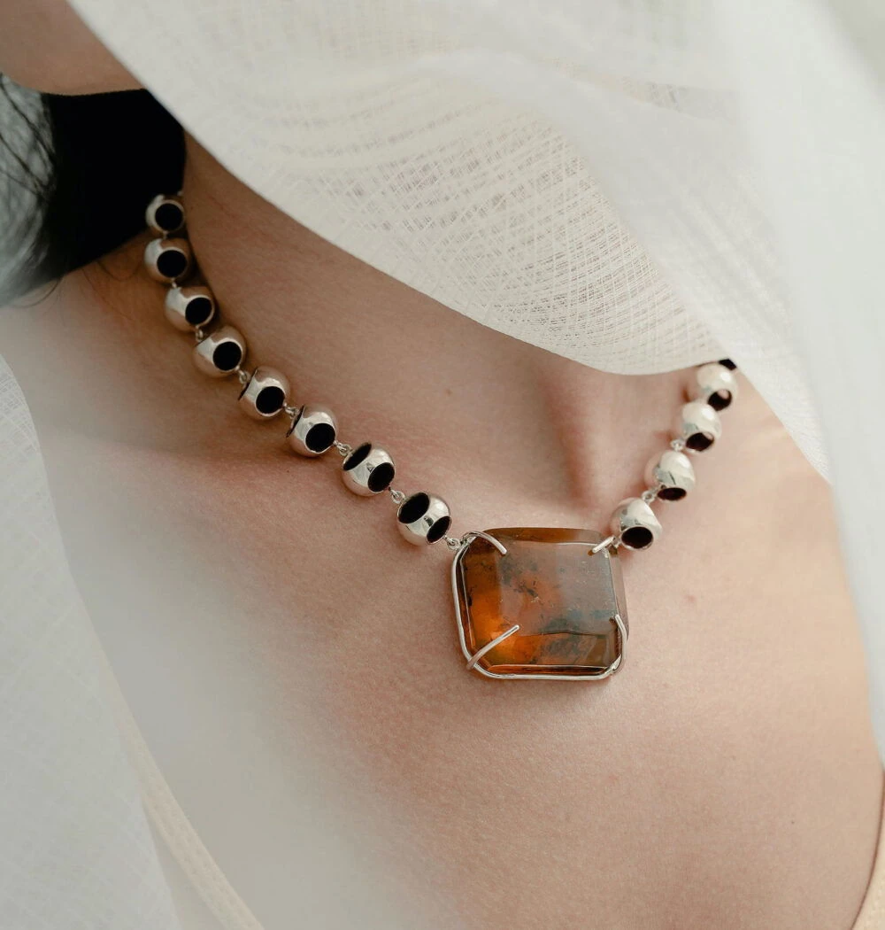 Close-up of a stylish amber choker necklace featuring a large rectangular amber pendant with silver links, on a woman's neck.