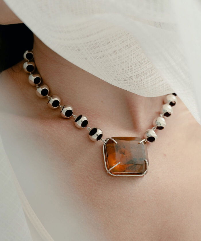 Close-up of a stylish amber choker necklace featuring a large rectangular amber pendant with silver links, on a woman's neck.