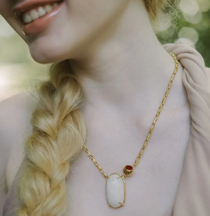 Elegant gold chain with a white moonstone pendant and red accent gemstone. Perfect for stylish jewelry lovers.
