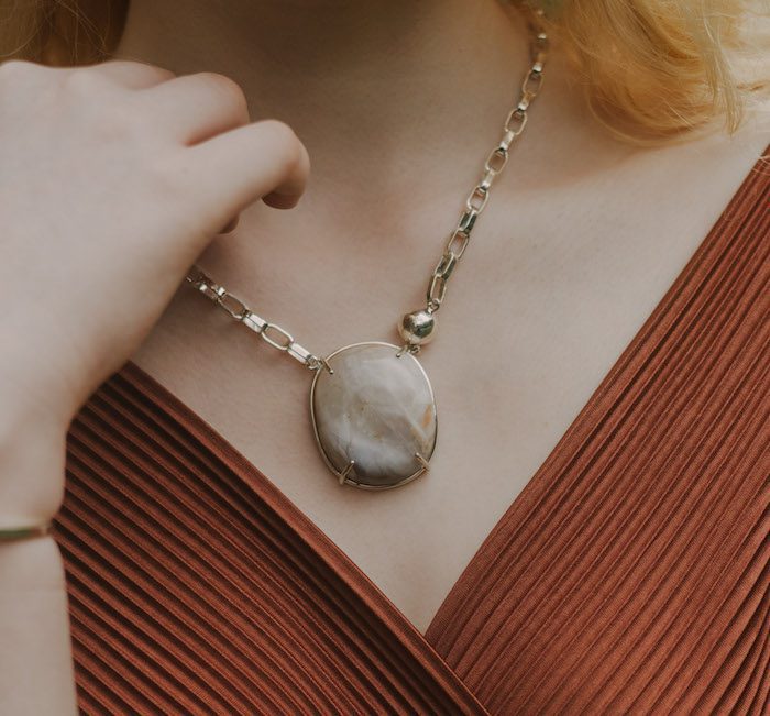 Close-up of moonstone pendant necklace worn with orange dress, sophisticated jewelry for women.