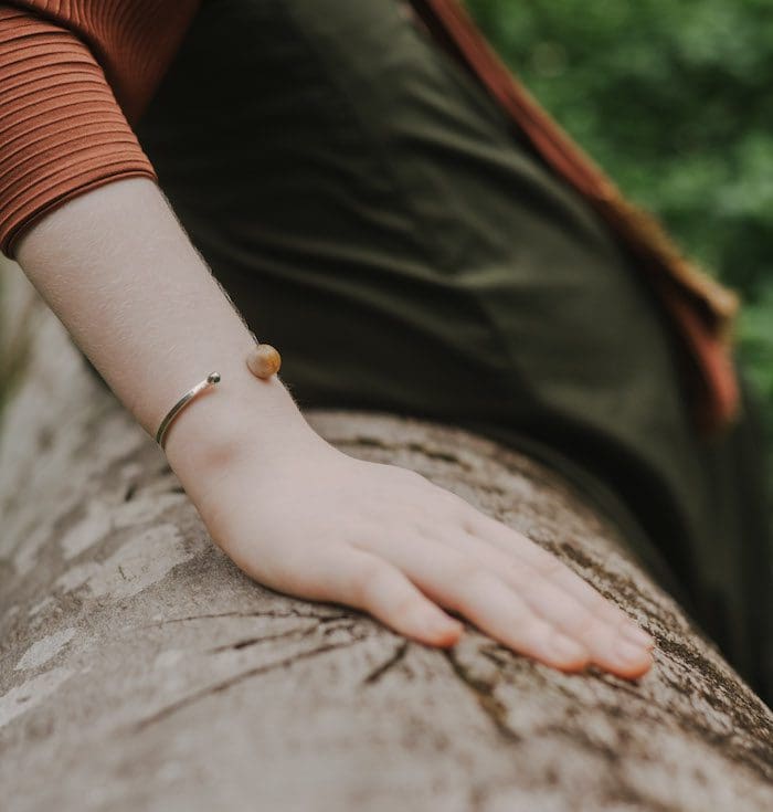 Elegant moonstone cuff bracelet on a woman's wrist, highlighting delicate jewelry and natural outdoor setting.