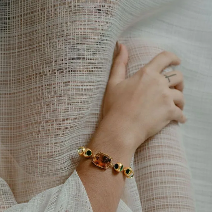 Delicate amber bracelet with gold beads on a woman's wrist, styled with a light, textured fabric.