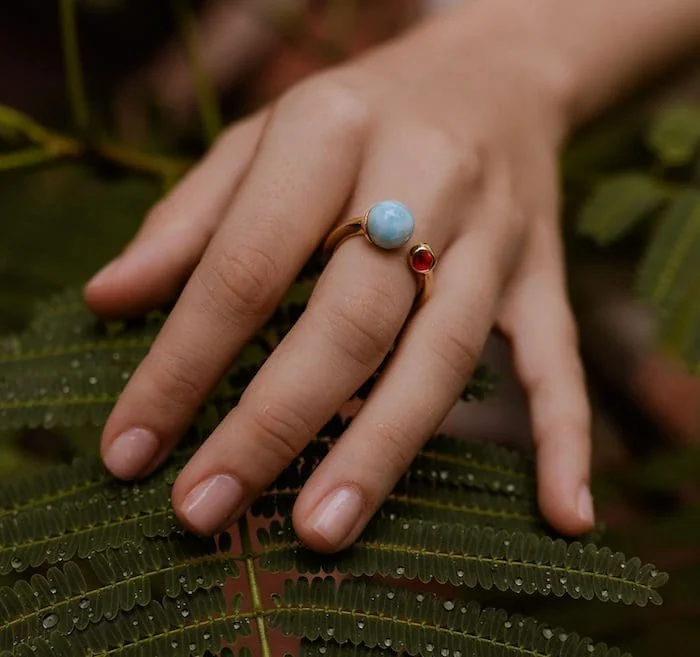 Delicate larimar and red gemstone ring on a woman's finger. Elegant jewelry piece with natural blue and red stones.