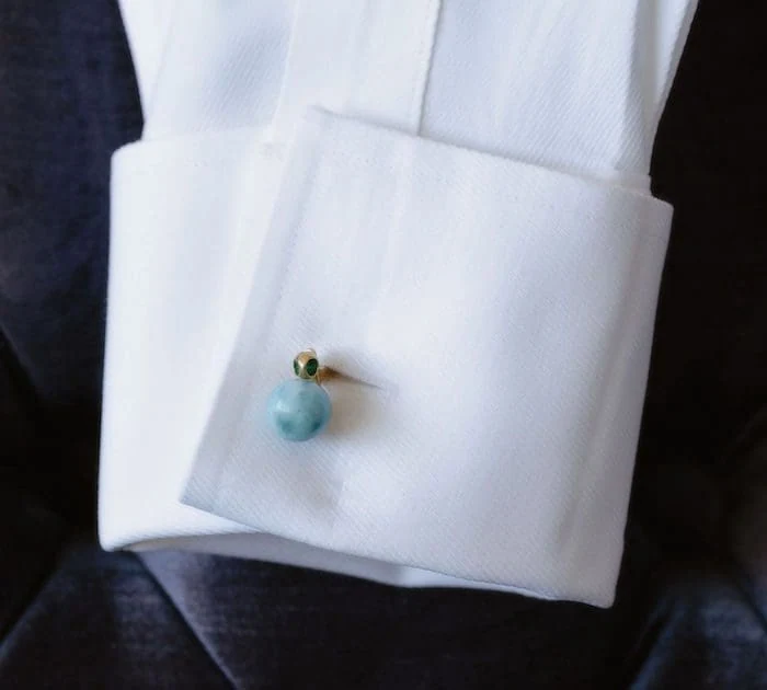 Larimar cufflink featuring a blue-green larimar gemstone in a gold setting on white dress shirt.