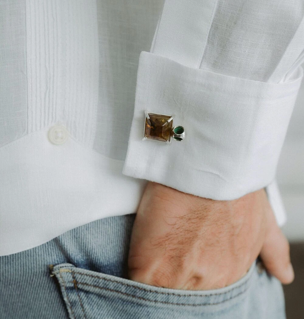 Close-up of cufflinks with amber and green stones on white shirt cuff for men.