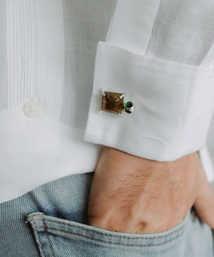 Close-up of cufflinks with amber and green stones on white shirt cuff for men.