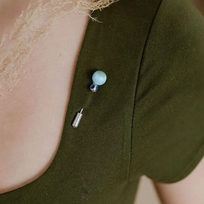 Close-up of a turquoise larimar gemstone pin on green fabric shirt. Elegant jewelry accessory highlighting blue mineral.