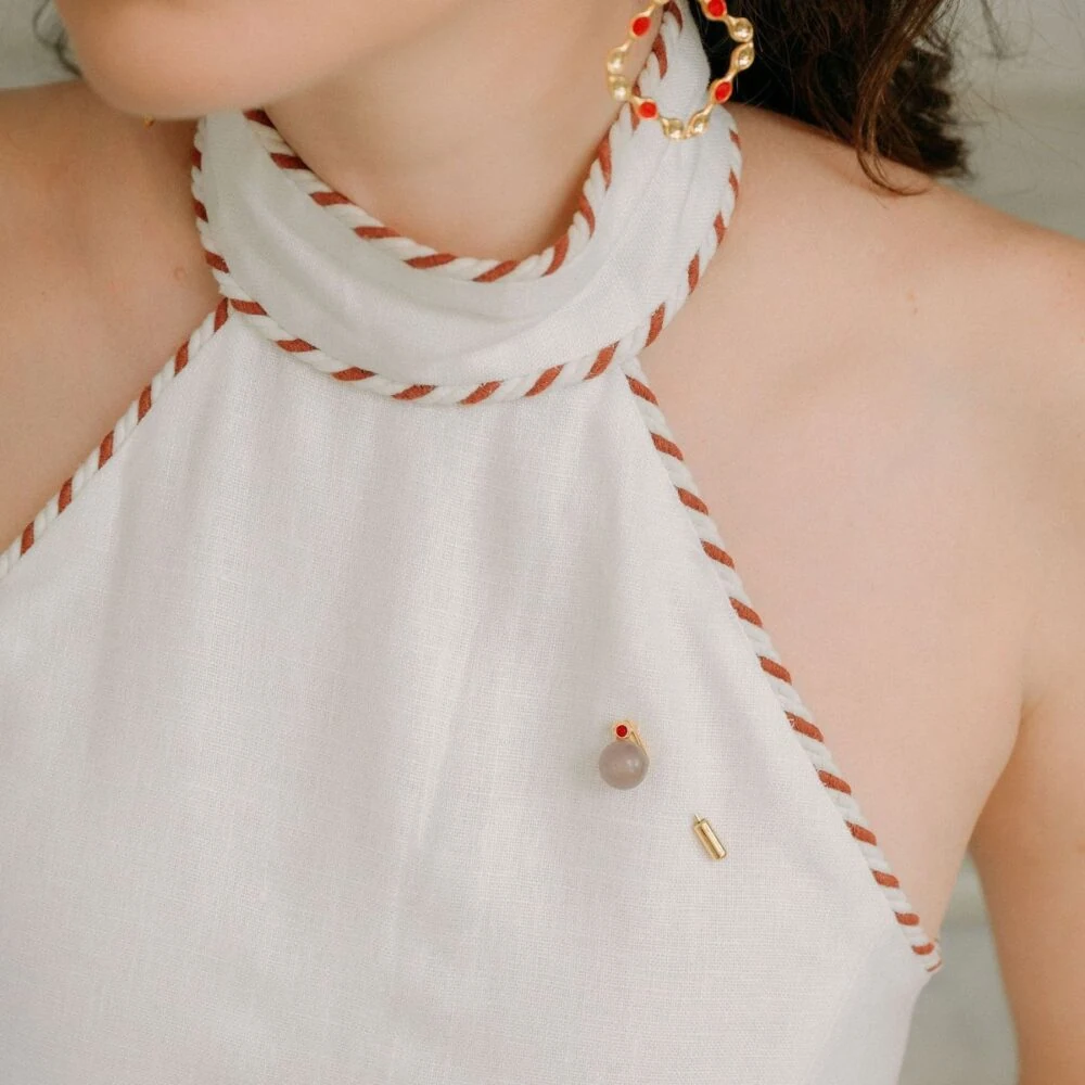 Pearl and gold jewelry pin on white top with red accents, stylish and sophisticated accessory.