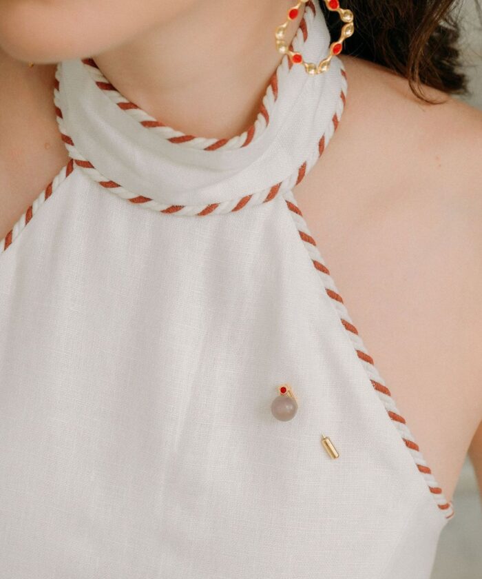 Pearl and gold jewelry pin on white top with red accents, stylish and sophisticated accessory.